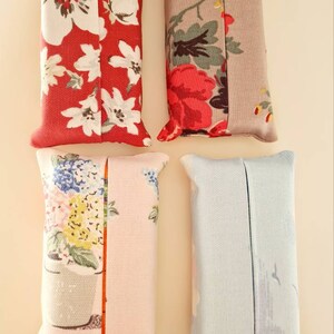 Pode incluir: Quatro capas de caixa de len&ccedil;os de tecido. Uma &eacute; vermelha com flores brancas, outra &eacute; cinza com flores vermelhas e brancas, outra &eacute; rosa com flores azuis e amarelas, e outra &eacute; azul claro.