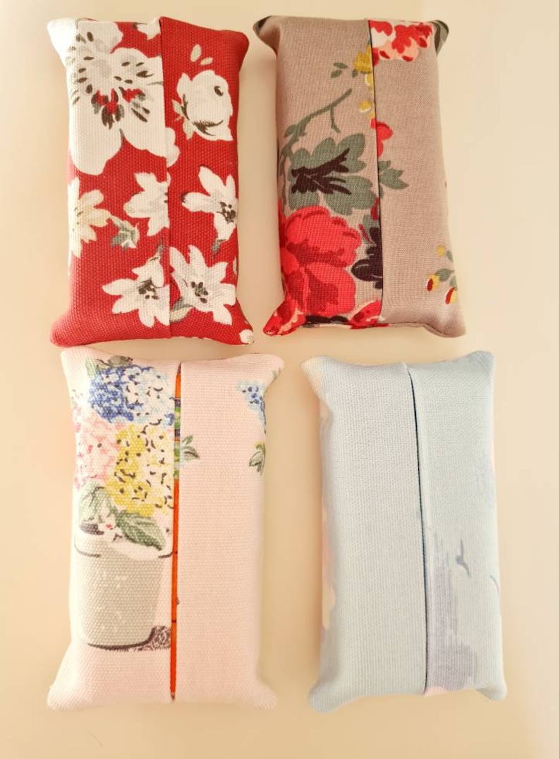 Pode incluir: Quatro capas de caixa de len&ccedil;os de tecido. Uma &eacute; vermelha com flores brancas, outra &eacute; cinza com flores vermelhas e brancas, outra &eacute; rosa com flores azuis e amarelas, e outra &eacute; azul claro.