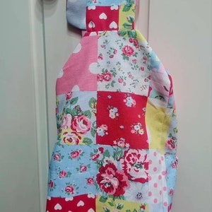 May include: A patchwork fabric bag with a pink, blue, and yellow floral pattern. The bag has a pink hood and two metal rings on the straps.