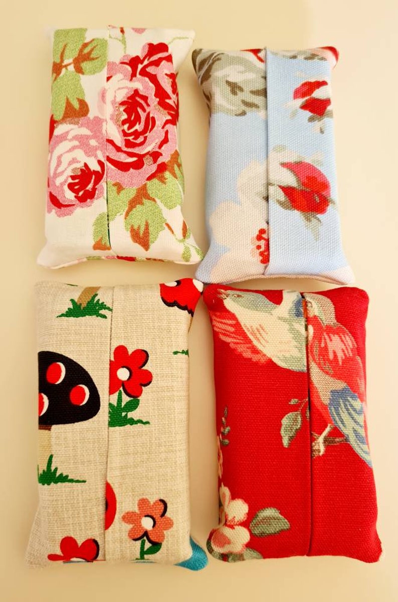 Pode incluir: Quatro capas de caixa de len&ccedil;os de tecido. Uma &eacute; floral com rosas cor-de-rosa e vermelhas sobre um fundo branco. Uma &eacute; azul com um padr&atilde;o floral branco e vermelho. Uma &eacute; bege com cogumelos vermelhos e pretos e flores vermelhas. Uma &eacute; vermelha com um p&aacute;ssaro branco e um padr&atilde;o floral.