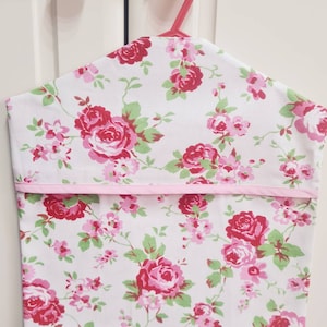 May include: A white fabric hanging organizer with a pink floral pattern. The organizer has a pink trim and is hanging on a red hanger.