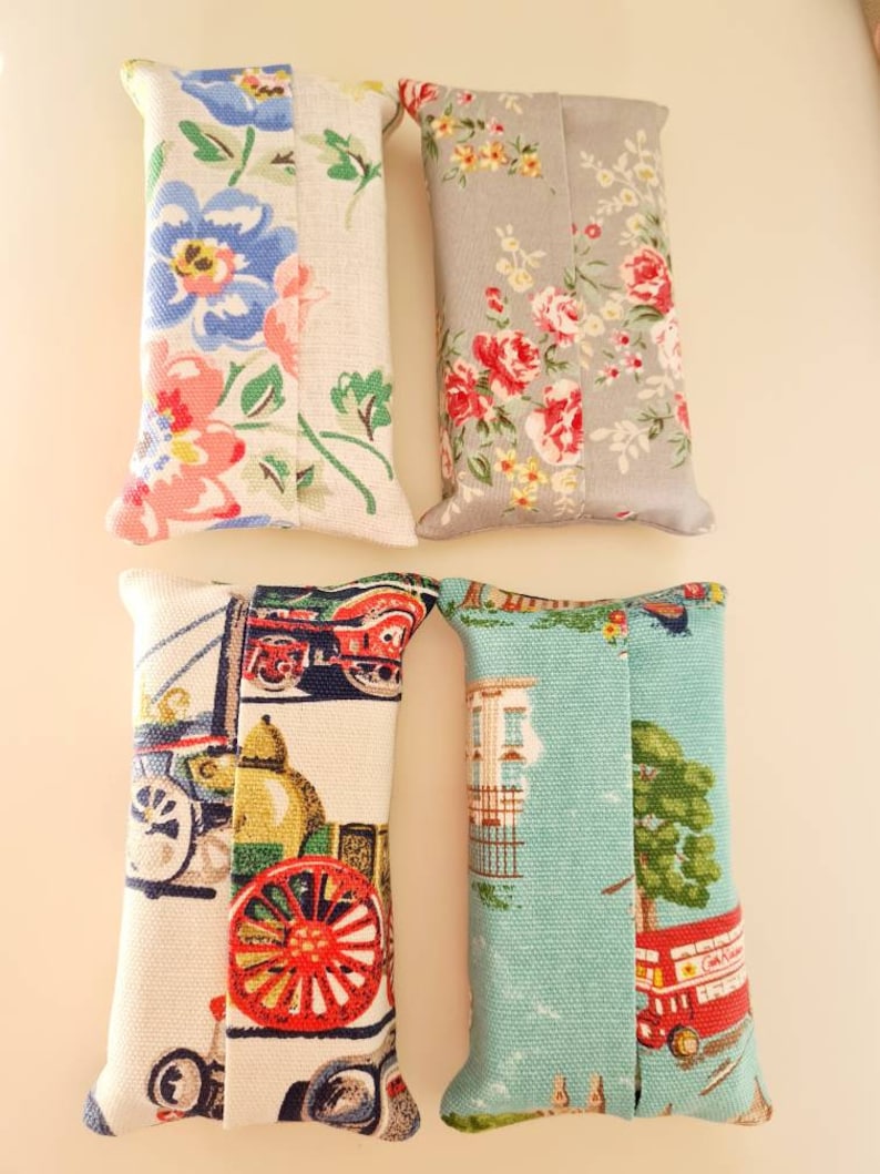 Pode incluir: Quatro capas de tecido para caixa de len&ccedil;os de papel. Uma &eacute; floral com flores rosa, azuis e verdes sobre um fundo branco. Outra &eacute; floral com flores rosa, vermelhas e amarelas sobre um fundo cinza. Uma &eacute; branca com um design de carro vintage vermelho, azul e verde. Outra &eacute; azul com um design de &ocirc;nibus de dois andares vermelho e uma &aacute;rvore verde.