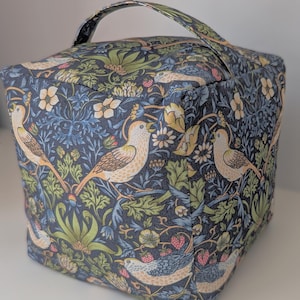May include: A square fabric storage box with a handle, patterned with birds, flowers, and foliage in blue, green, and cream. The box is designed for storage and organisation, and is ideal for a bedroom or living room.
