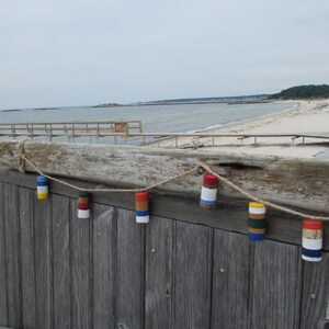 May include: A wooden fence with a string of colorful, painted, cork buoys hanging from it. The buoys are red, white, blue, yellow, and green.