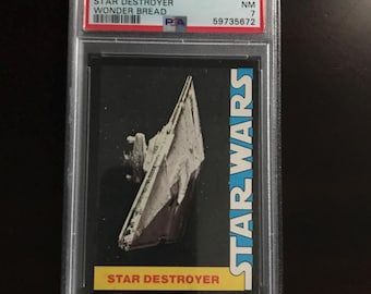 Puede incluir: Una tarjeta coleccionable calificada con un Star Destroyer de la serie Star Wars de 1977. La tarjeta, en un soporte protector, muestra el texto "STAR DESTROYER" y "STAR WARS". La tarjeta está calificada y etiquetada con un número y condición.