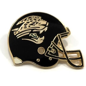 May include: A black and gold enamel pin shaped like a football helmet. The helmet features a gold jaguar head logo on the side and a gold-colored facemask. The pin is set against a white background.