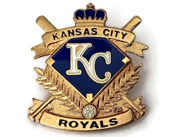 Puede incluir: Pin dorado de los Reales de Kansas City. El pin presenta un diamante azul con las letras "KC" en blanco. Las palabras "Kansas City" y "Royals" se muestran en dorado, con bates de béisbol cruzados y una corona.