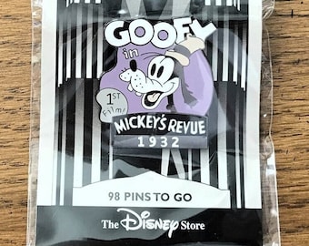 Może przedstawiać: Czarno-biała przypinka przedstawiająca Goofy'ego w fioletowym kostiumie z napisem "Goofy in Mickey's Revue 1932". Przypinka jest częścią serii Countdown to the Millennium 2000 i zawiera napis "98 Pins to Go" oraz "The Disney Store".