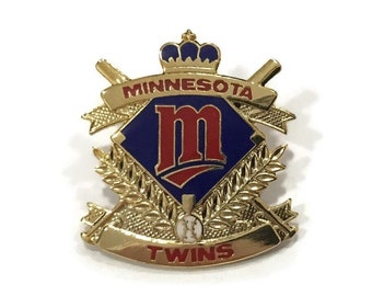 Puede incluir: Pin de béisbol de los Minnesota Twins de color dorado con un logotipo "M" azul y rojo, una pelota de béisbol y las palabras "Minnesota Twins".