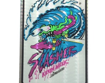 Puede incluir: Una pegatina holográfica con un monstruo de dibujos animados en monopatín en una ola. El monstruo es verde y azul con una lengua rosa. La palabra "SLASHER" está en rosa, con "KEVIN MEEK" y "SANTA CRUZ" debajo.