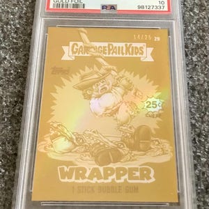 May include: A gold foil Garbage Pail Kids trading card, graded and encased. The card features an illustration of a character with a hat and a weapon, with the text "WRAPPER" and "1 STICK BUBBLE GUM". The card is labeled "2024 GPK GAME OVER LEVEL 2".