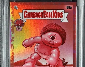 Może przedstawiać: Karta kolekcjonerska Garbage Pail Kids 40th Anniversary 2025, #88a Sy Clops, edycja Ruby, numerowana 07/40, certyfikowana przez PSA. Karta przedstawia różowego, jednookiego cyklopa w pieluszce na metalicznym, holograficznym czerwonym tle.