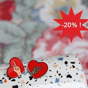 May include: Two red heart-shaped enamel pins with a hand giving the middle finger. One pin features a light skin tone hand, the other a dark skin tone hand. A red starburst graphic with the text "-20% !" is also visible.