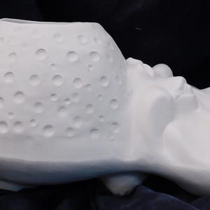 May include: A white ceramic vase with a textured surface and a series of small, evenly spaced indentations. The vase has a bulbous shape with a wide opening at the top and a sculpted, organic form on the side.
