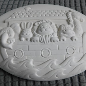 May include: Oval-shaped, unpainted ceramic plaque depicting Noah's Ark. The ark features a roof, animals, and waves. Animals include an elephant, rabbit, lion, hippo, and giraffe. The plaque is designed for painting.