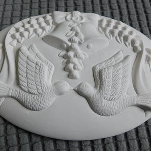 May include: White oval-shaped relief sculpture featuring two doves kissing, with detailed wing and tail feathers. Above the doves are two bells and floral accents, suggesting a wedding or celebration theme.