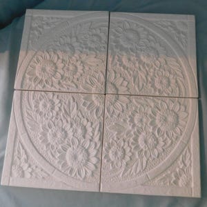 May include: Four square white tiles arranged in a grid, each featuring a raised relief design of sunflowers and leaves within a circular border. The matte white surface highlights the intricate floral textures and the geometric layout of the set.