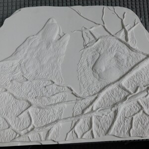 May include: A white, rectangular relief sculpture featuring two wolves. One wolf is howling, and the other is looking forward. The wolves are surrounded by branches. The sculpture has a textured surface.