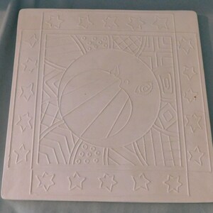 May include: A square white ceramic tile featuring an embossed design of a central moon with a face, surrounded by geometric patterns including circles, lines, and grids. The border of the tile is decorated with a repeating pattern of stars.