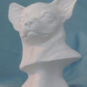 May include: A matte white ceramic bust sculpture depicting the head and neck of a chihuahua dog. The piece features detailed molded fur texture, large upright ears, and a defined snout, presented as a solid, unpainted monochromatic figurine.