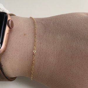 May include: A gold chain bracelet on a person's wrist.