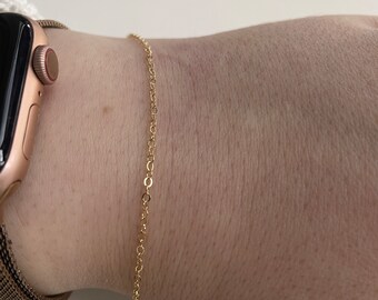May include: A gold chain bracelet on a person's wrist.