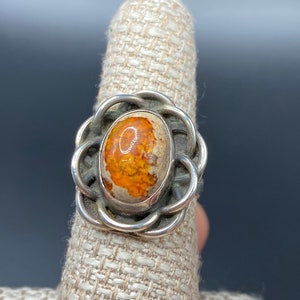 May include: A silver ring with an oval-shaped orange and white gemstone set in a delicate, intricate design.