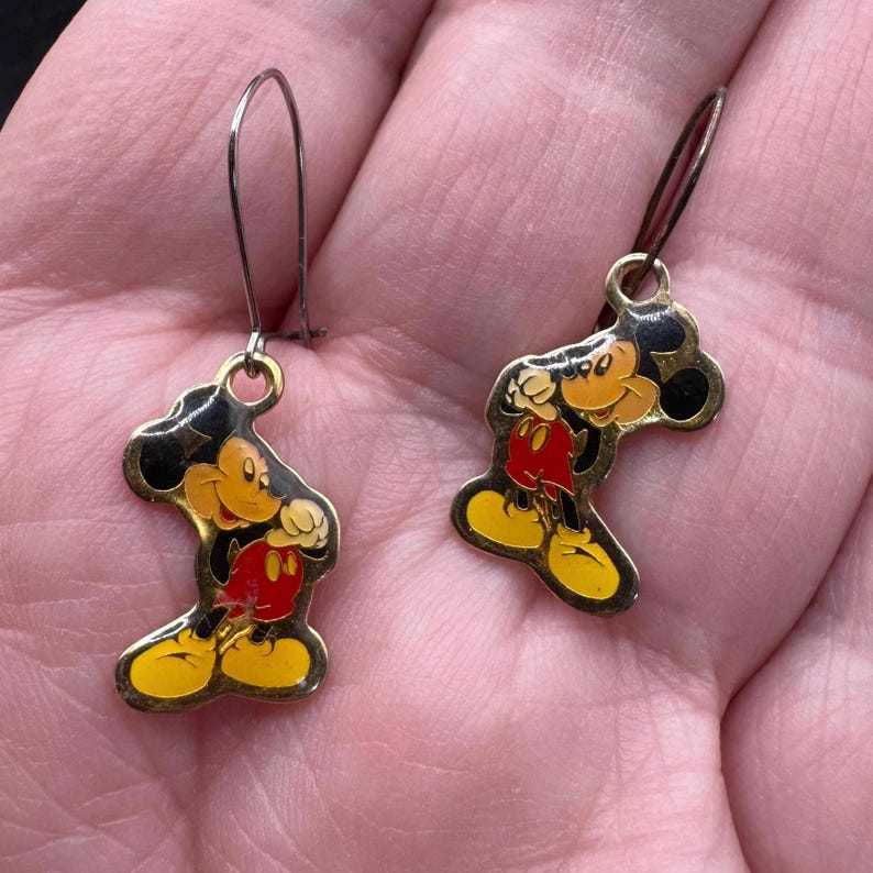 K&ouml;nnte beinhalten: Ein Paar Vintage-Ohrringe mit Mickey Mouse. Jeder Ohrring hat eine goldfarbene Metallkontur mit einem schwarzen, roten, gelben und beigefarbenen Emaille-Mickey-Mouse-Design. Die Ohrringe haben einen einfachen Hakenverschluss.