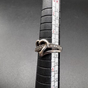May include: A silver ring with a heart design and small clear stones. The ring is on a sizing tool and measures size 6.