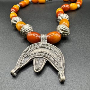 May include: A necklace with amber beads and a large silver pendant. The pendant is shaped like a crescent moon with intricate designs.