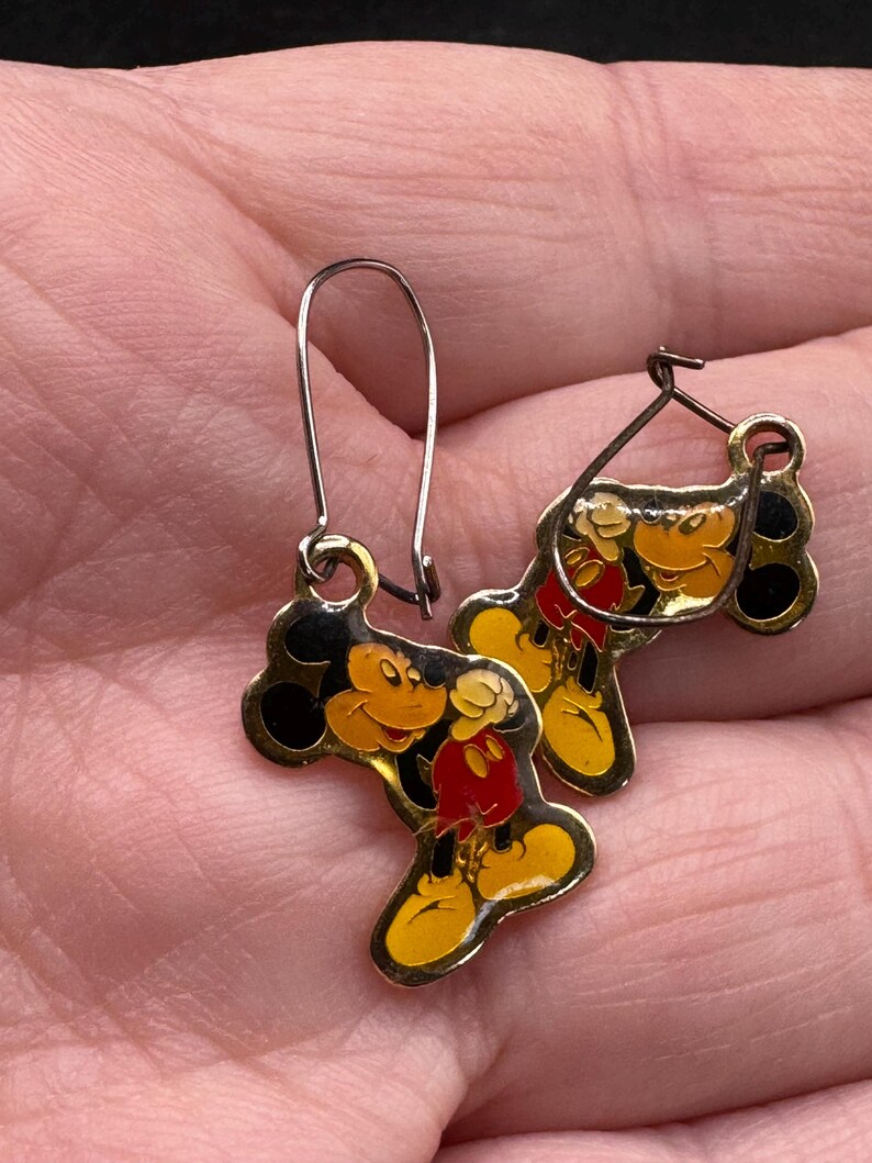 K&ouml;nnte beinhalten: Ein Paar Vintage-Mickey-Mouse-Ohrringe. Die Ohrringe haben eine goldfarbene Metallkontur mit Emaille-Details in Schwarz, Gelb und Rot. Sie haben einen Hakenverschluss.