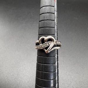 May include: A silver ring with a heart-shaped design and a row of small diamonds.