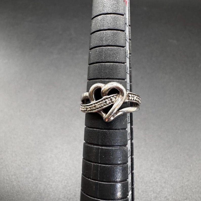 May include: A silver ring with a heart-shaped design and a row of small diamonds.