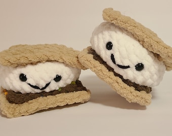 May include: Two plush s'mores with smiling faces. The s'mores are made of brown graham cracker, white marshmallow, and brown chocolate.
