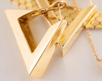 May include: A pair of gold triangle-shaped earrings with a hinge closure. The earrings are on a white surface.