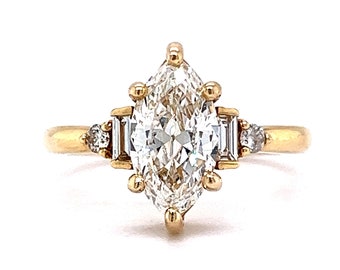 Pode incluir: Um anel de noivado de ouro com um grande diamante em forma de marquesa e dois diamantes menores em forma de baguette de cada lado.