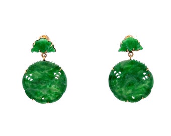 May include: A pair of green jade earrings with gold accents. The earrings feature a round jade pendant with intricate carvings and a smaller jade piece shaped like a leaf.