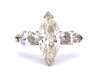 Puede incluir: Un anillo de plata con un gran diamante de forma marquesa en el centro y dos diamantes de forma marquesa más pequeños a cada lado.