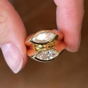 Pu&ograve; includere: Un anello d'oro con due diamanti a forma di marquise incastonati al centro. L'anello &egrave; progettato con una fascia curva.