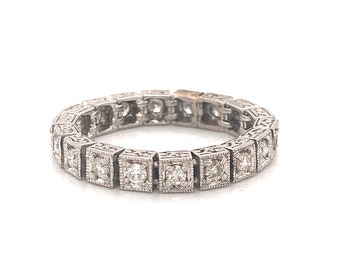 Könnte beinhalten: Ein silberfarbener Eternity-Ring bestehend aus einer Reihe quadratischer Glieder, die jeweils einen einzelnen runden, klaren Stein enthalten. Der Metallrahmen weist an den Kanten jeder quadratischen Fassung feine Milgrain-Details auf.