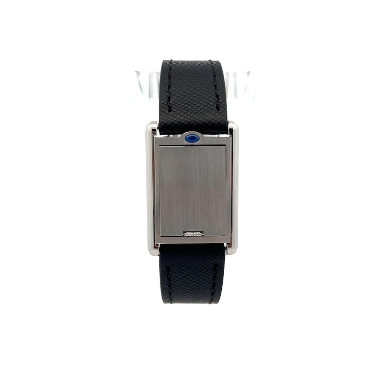 May include: Close-up view of a rectangular wristwatch with a sleek, silver-toned case and a black leather strap. The watch face is concealed behind a silver-toned cover, and a small, dark blue gemstone is visible near the top of the case. The watch has a minimalist design, and the strap appears to be made of textured leather. The overall style suggests a modern and sophisticated timepiece.