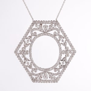 May include: A silver pendant necklace with a hexagonal frame set with small diamonds. The frame features a delicate floral design and a large oval opening in the center.