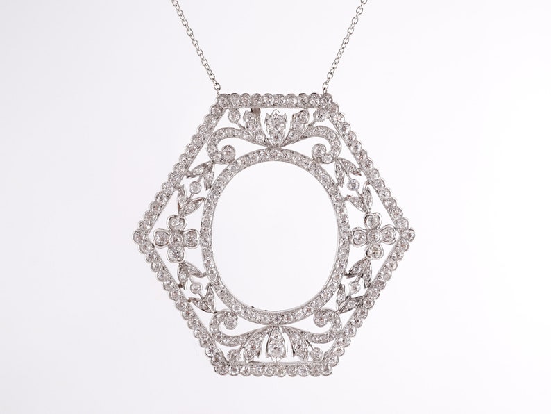 May include: A silver pendant necklace with a hexagonal frame set with small diamonds. The frame features a delicate floral design and a large oval opening in the center.
