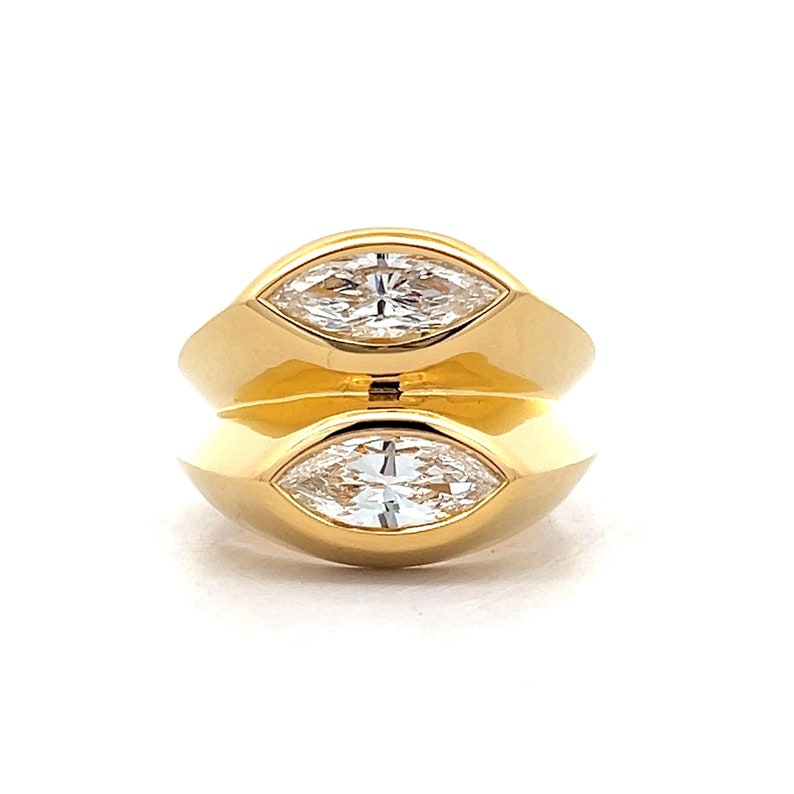 Pu&ograve; includere: Un anello d'oro con due diamanti a forma di marquise incastonati nella fascia. I diamanti sono trasparenti e brillanti.