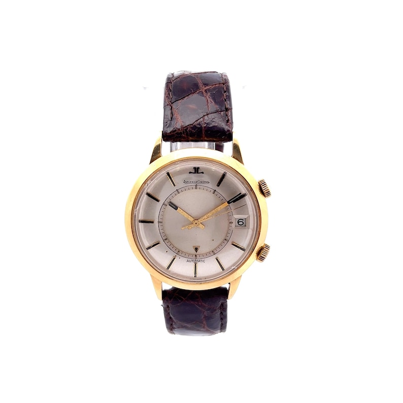 May include: A gold-tone wristwatch with a white face and black hands. The watch has a brown leather band and the words "Jaeger-LeCoultre" and "Automatic" are printed on the face.