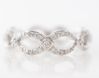 May include: A delicate white gold ring with a diamond-encrusted infinity design. The ring features a central diamond in a square shape, surrounded by smaller diamonds.