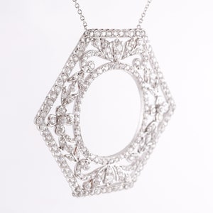 May include: A silver pendant necklace with a hexagonal frame set with small diamonds. The frame is designed with a floral pattern and has a circular opening in the center.