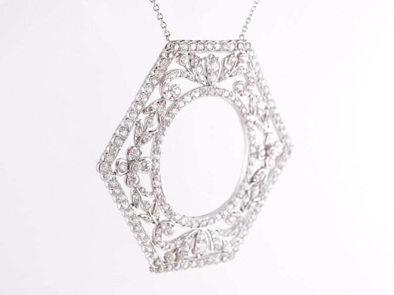 May include: A silver pendant necklace with a hexagonal frame set with small diamonds. The frame is designed with a floral pattern and has a circular opening in the center.