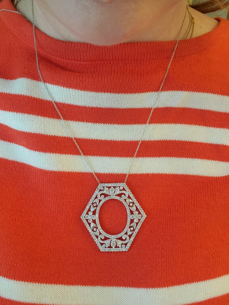 May include: A silver necklace with a hexagonal pendant featuring a detailed, ornate design with a circle in the center. The necklace is worn over a red and white striped sweater.