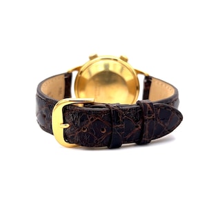 May include: A gold-tone wristwatch with a brown leather band. The watch has a round face and a chronograph function.